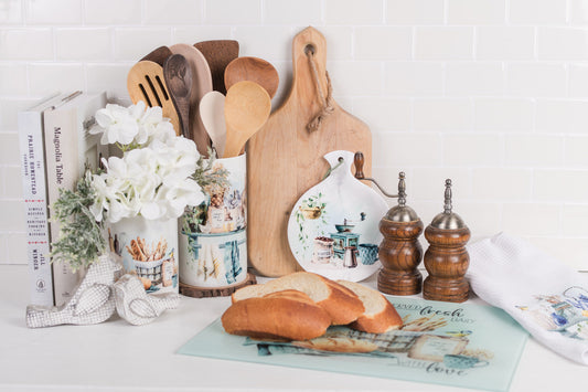 Country kitchen crock next to a glass, cutting board trivet canisters tea, towel, and cookbooks