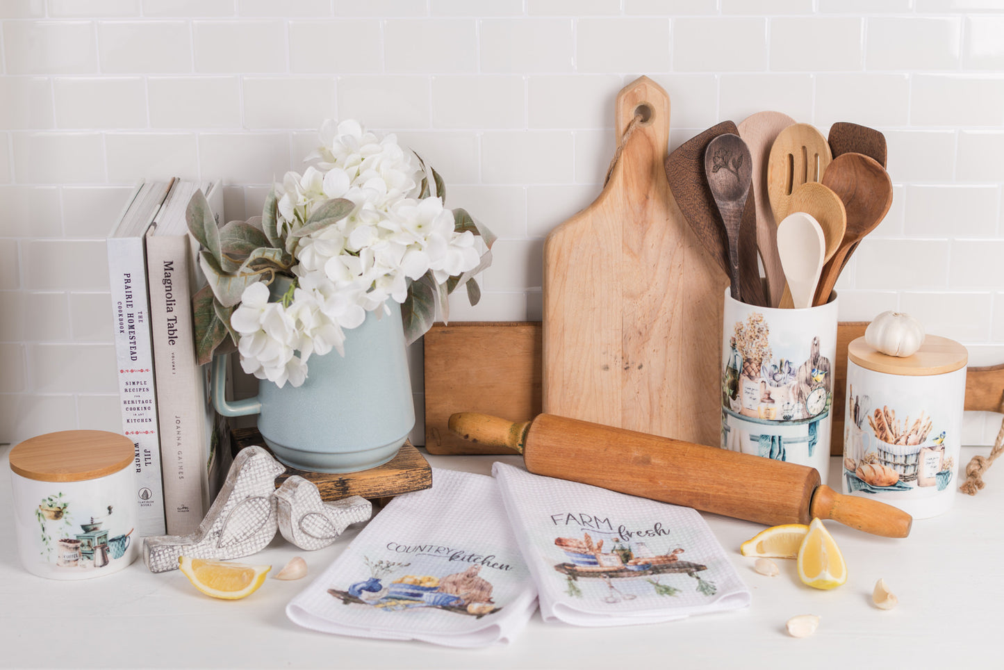 Country kitchen crock next to blue floral pitcher and rolling pin, and coordinating tea towels and canisters