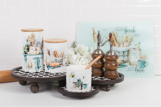 Small, medium, and large ceramic canisters with bamboo lids styled with a cutting board and salt and pepper mills.