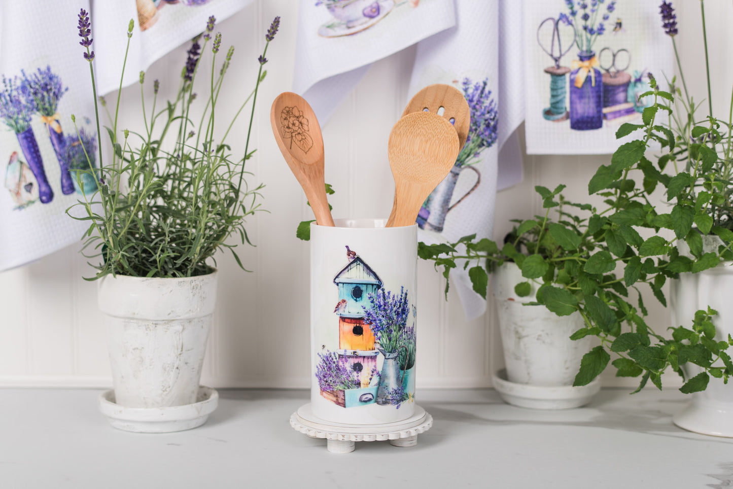 ceramic container with wooden spoons on a surface with plants and decorative items in the background