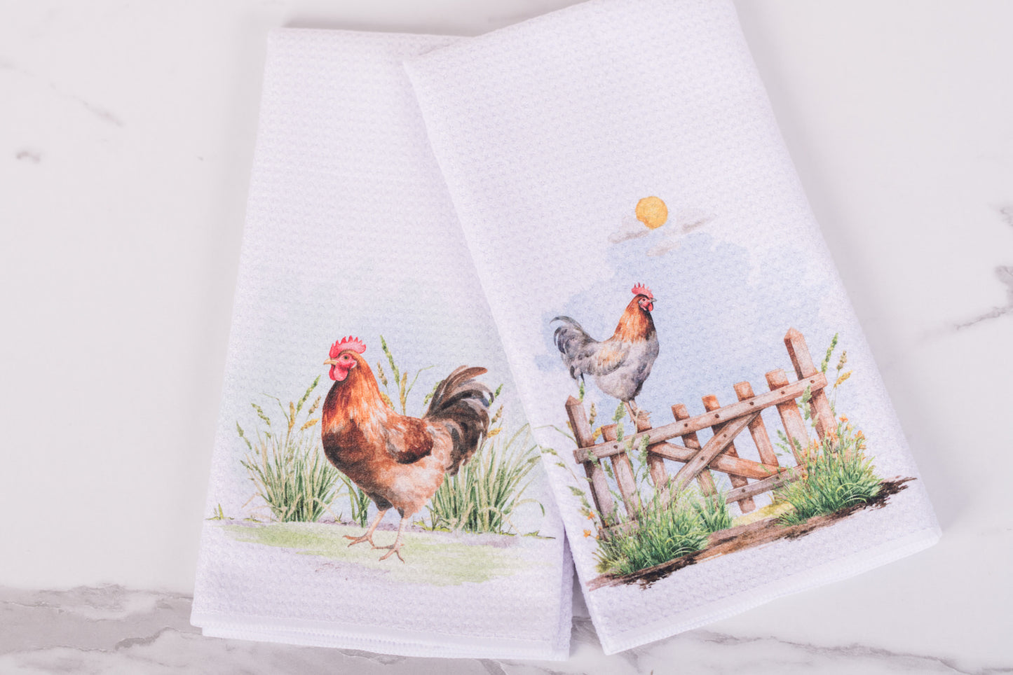 Two towels with farm-themed designs featuring chickens and a fence on a white background.