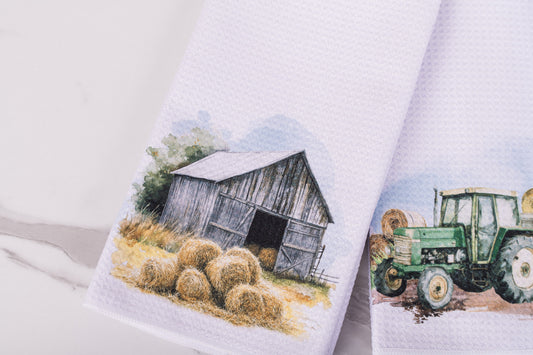 Two towels with farm-themed designs of a barn and tractor on a white background.