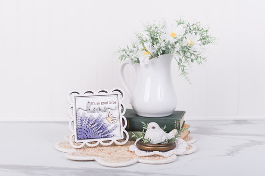 Decorative items including a white pitcher, DIY framed picture, and small bird figurine on a light surface.