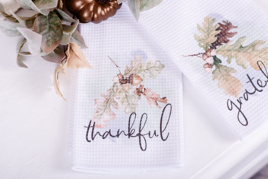 Thankful fall tea towel set from the Woodland Collection styled near a bronze pumpkin and leaves