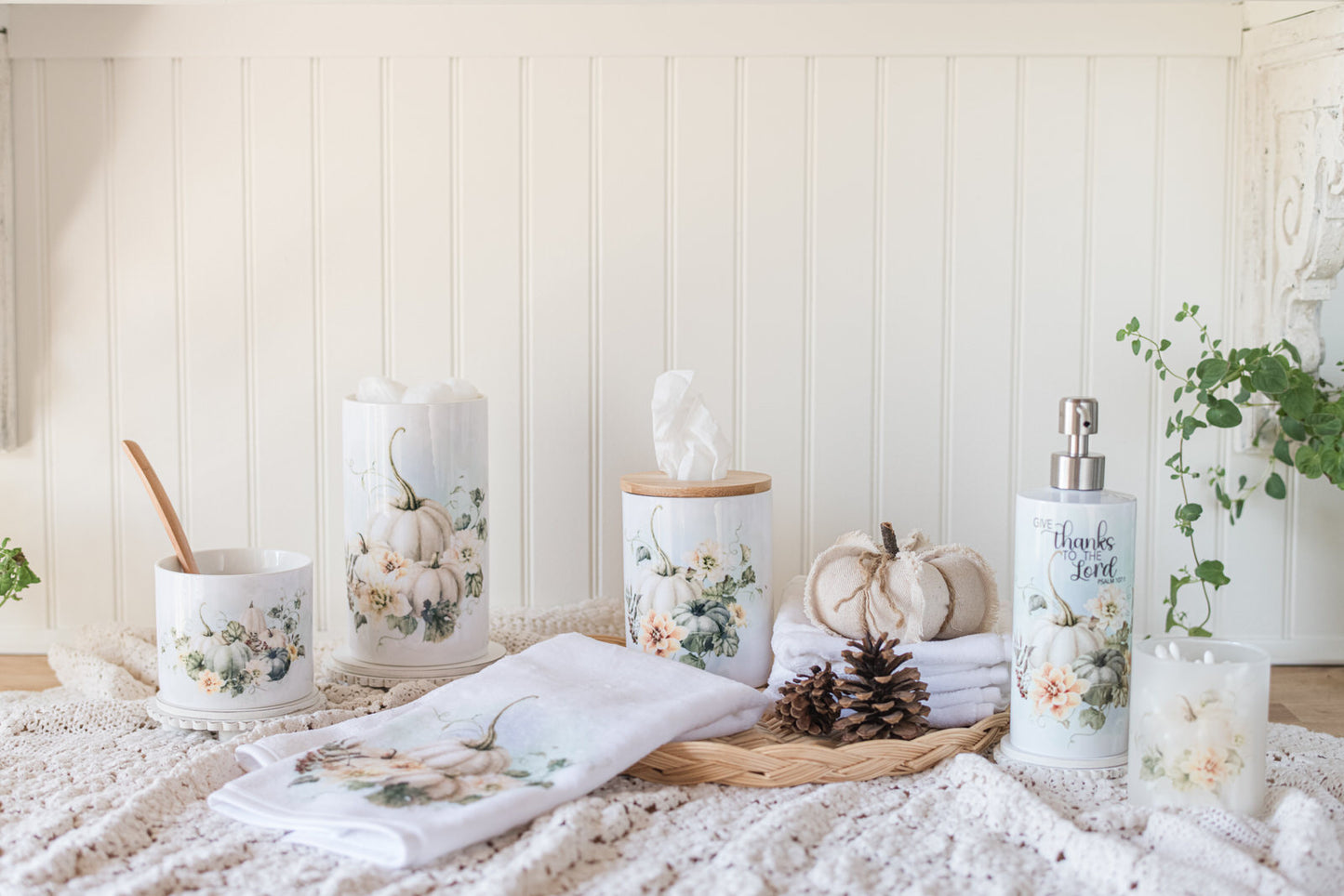 Decorative fall canisters styled for a bathroom with a ceramic tissue holder, hand towel, soap dispenser on a wicker tray with pinecones and a pumpkin