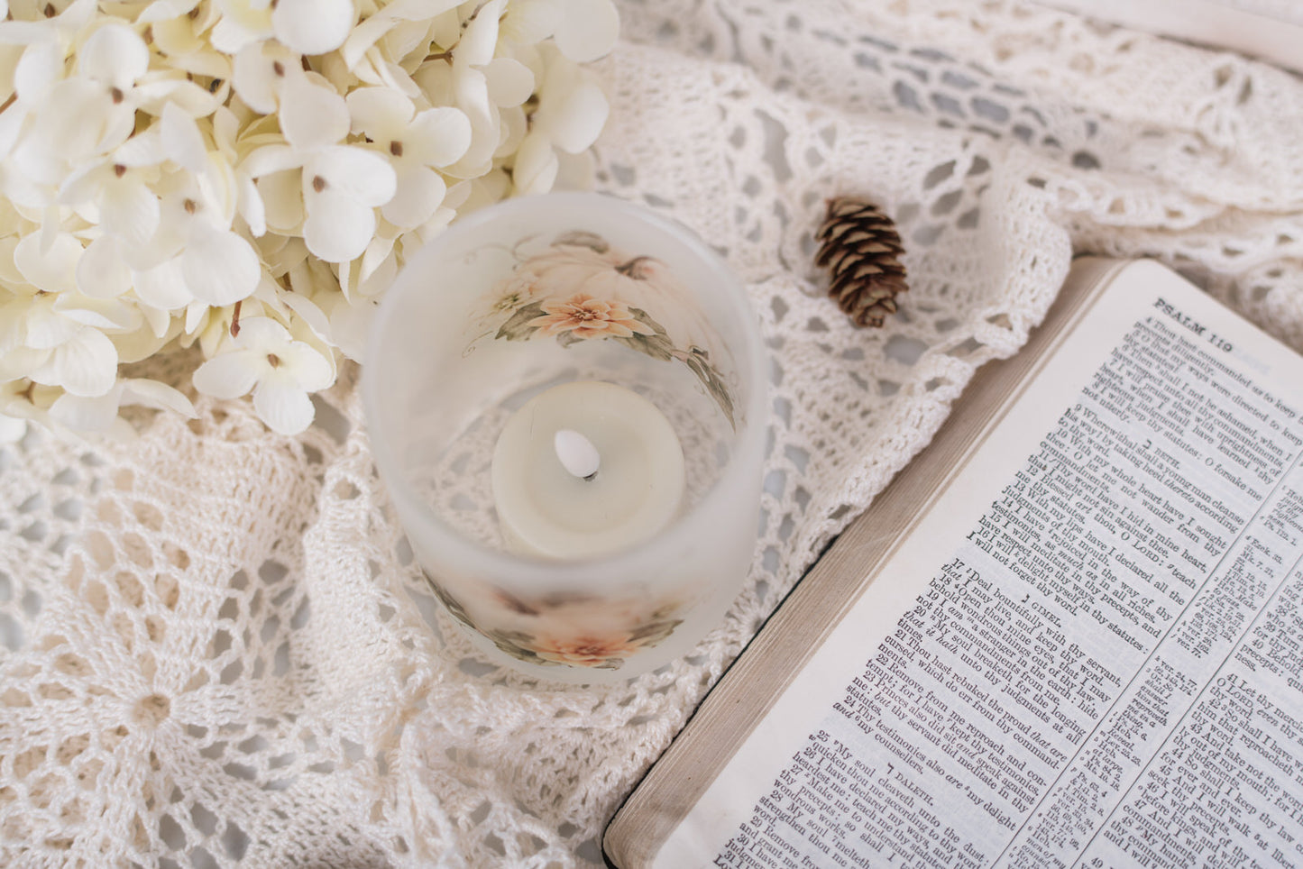Candle, white flowers, and an open bible on a lace surface