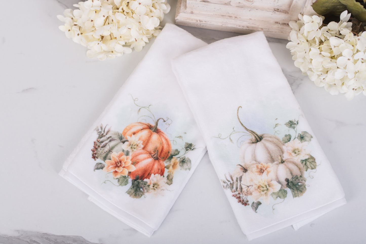 Two decorative towels with pumpkin and floral designs on a light surface.