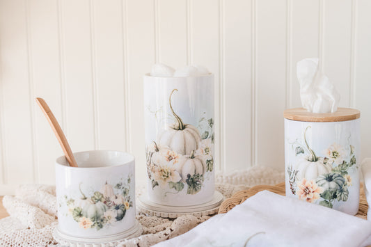 Decorative jars and ceramic tissue holder with floral and pumpkin designs on a textured surface.