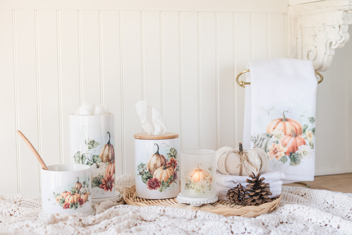 Decorative bathroom jars with a candle, a towel with autumn canisters on a counter with pumpkins and pinecones