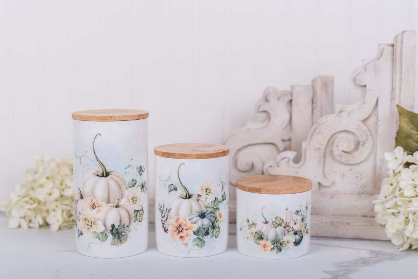 Three decorative bathroom canisters with floral and pumpkin designs on a white surface.