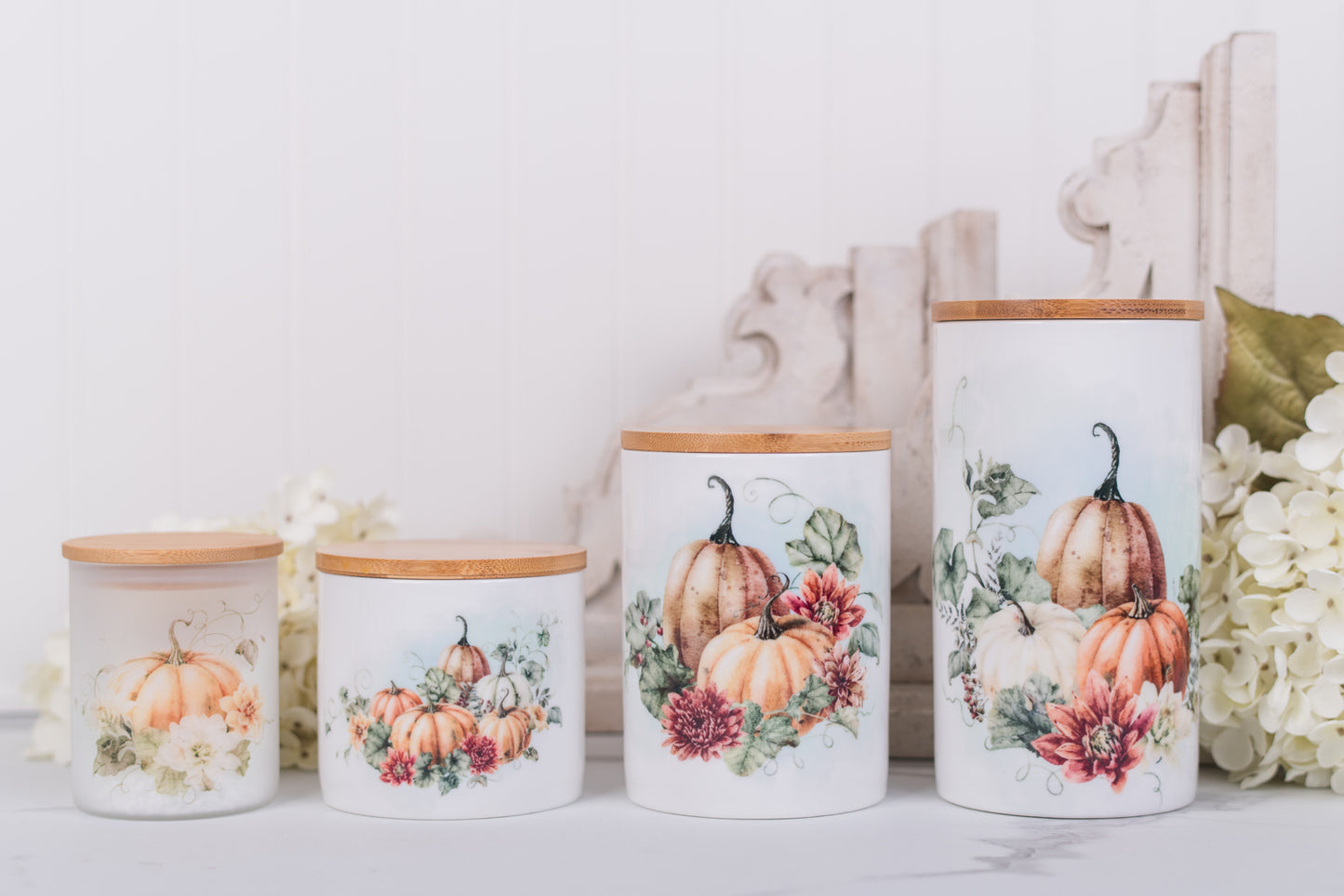 Set of ceramic bathroom canisters with warm, rich pumpkins and floral designs on a white surface with flowers.
