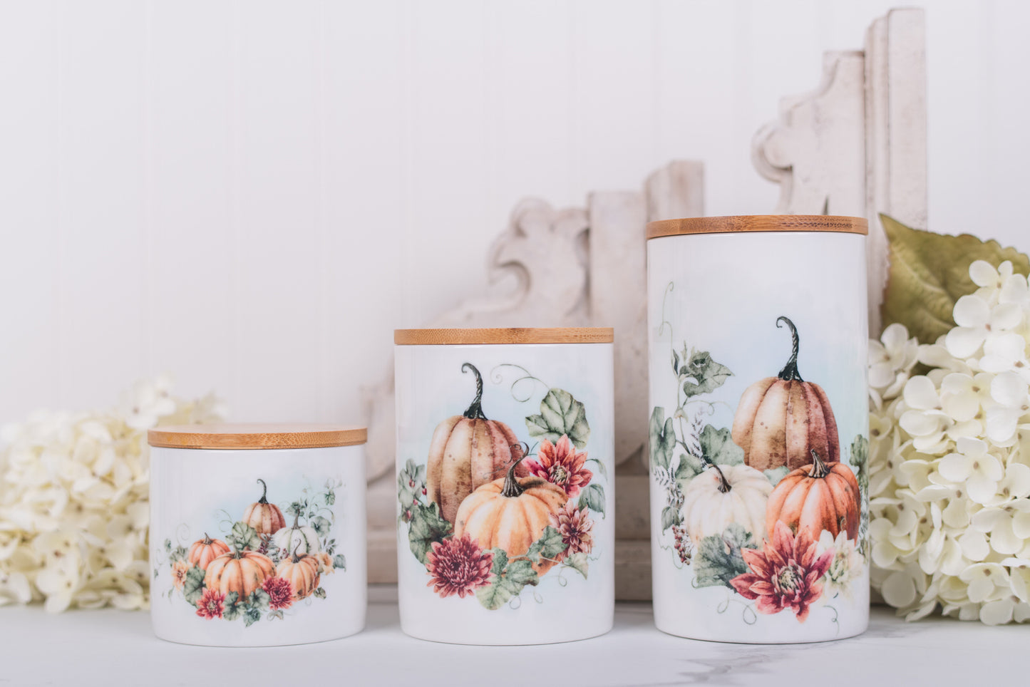 Set of three ceramic bathroom canisters with pumpkin and floral design on a white surface.