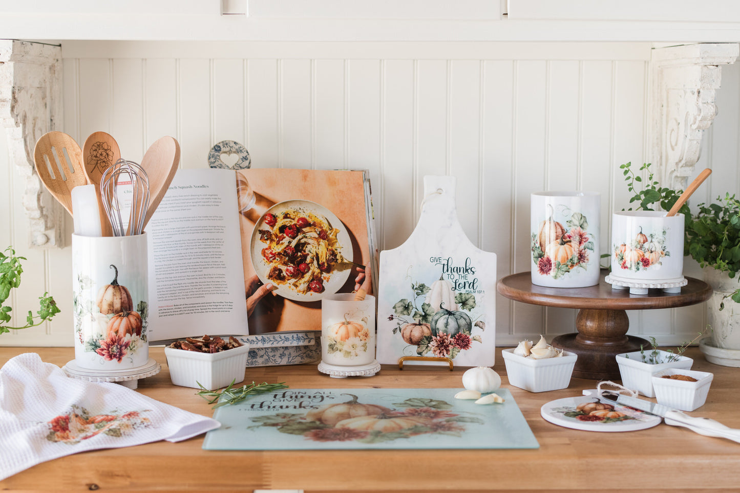 Decorative Fall kitchen items, including a cutting board, candles, and a cookbook, on a wooden butcher block