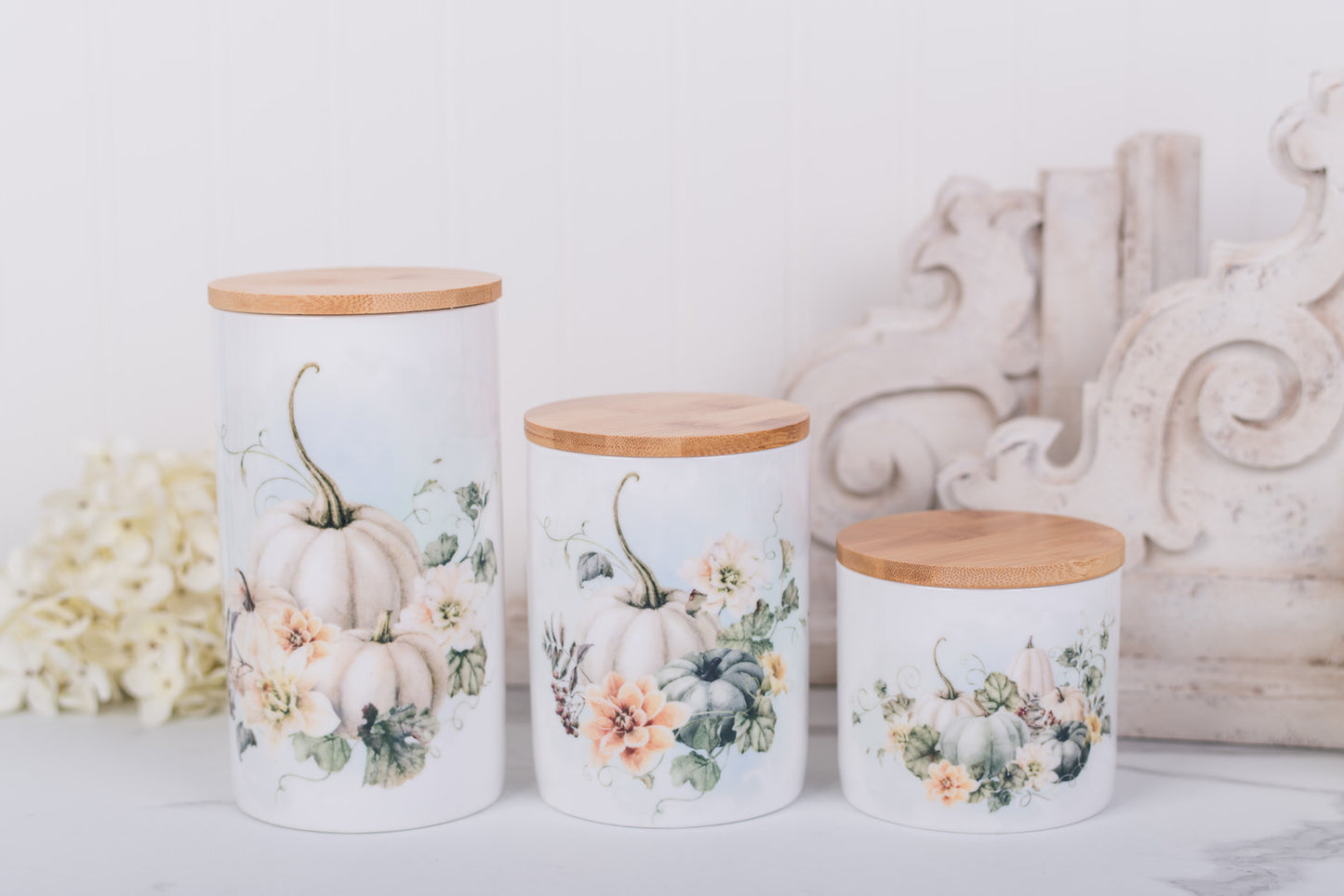 Three decorative canisters with floral and pumpkin designs on a white surface.