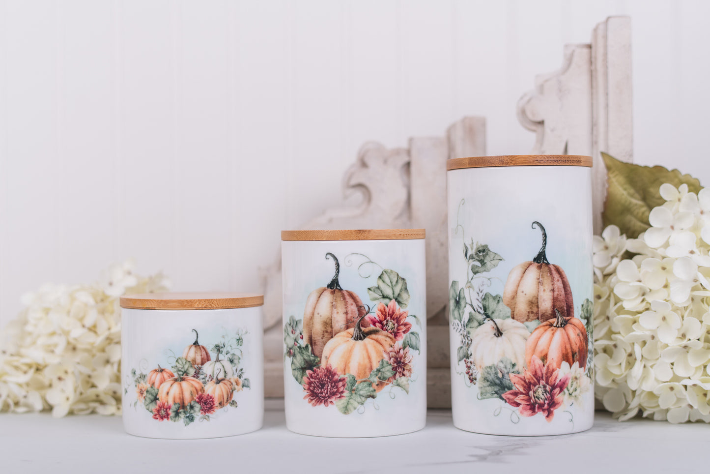 Set of ceramic canisters with pumpkin and floral design on a white surface with flowers.