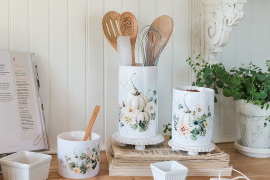 Decorative fall kitchen canisters and utensil holder with floral designs on a wooden surface.