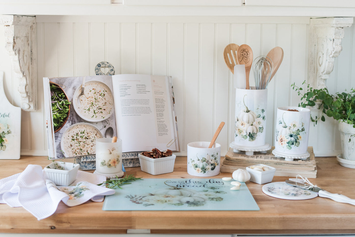 A kitchen counter styled for fall with cookbooks, utensils, a cutting board and decorative items on a wooden surface.