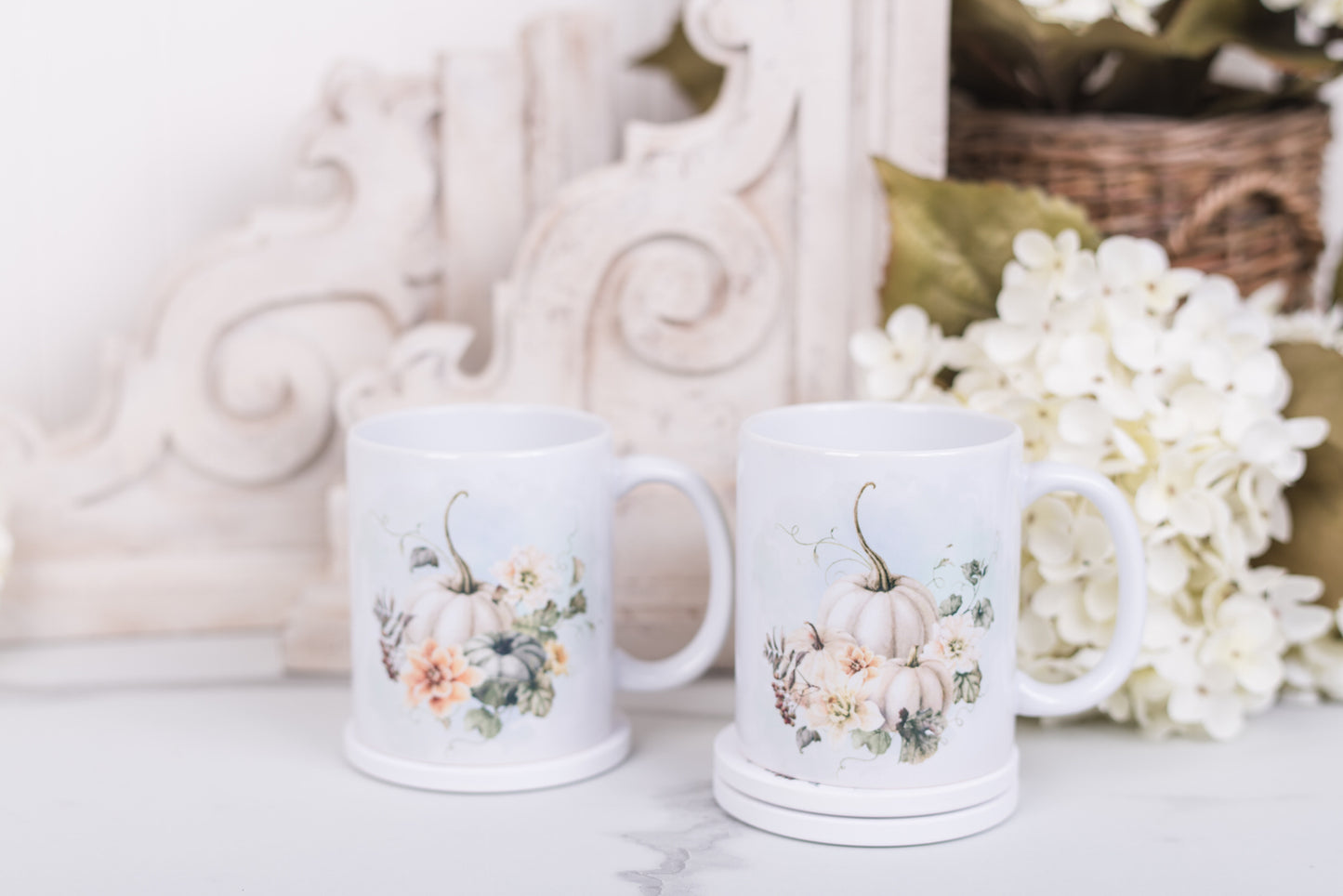 Two white mugs with pumpkin and floral designs on a marble counter