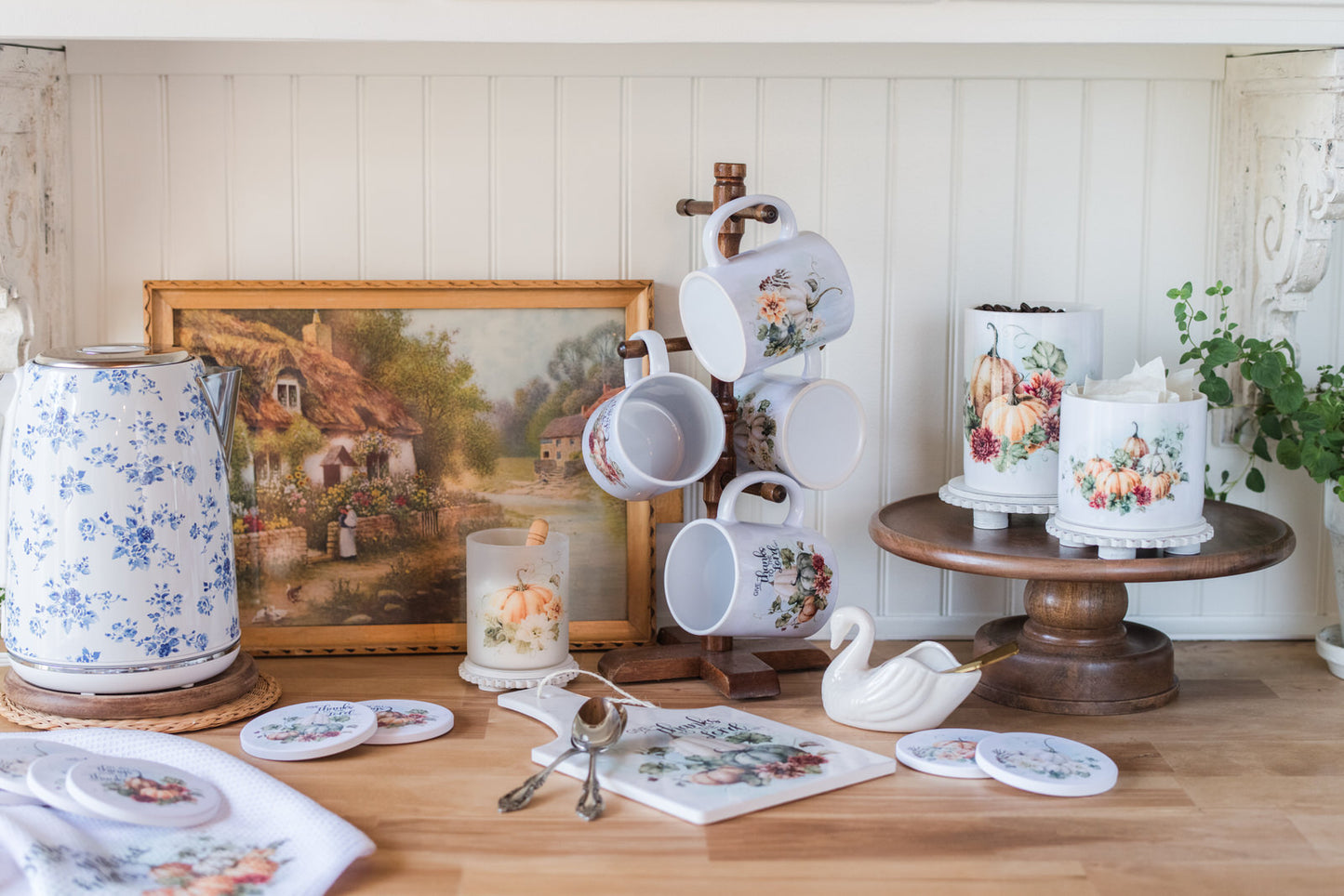 Collection of pumpkin and floral teaware on a wooden table with a scenic painting in the background.