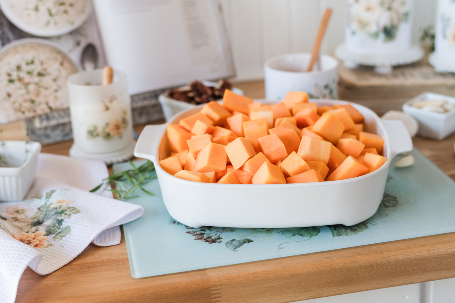 Diced squash in a white casserole dish on a glass cutting board.