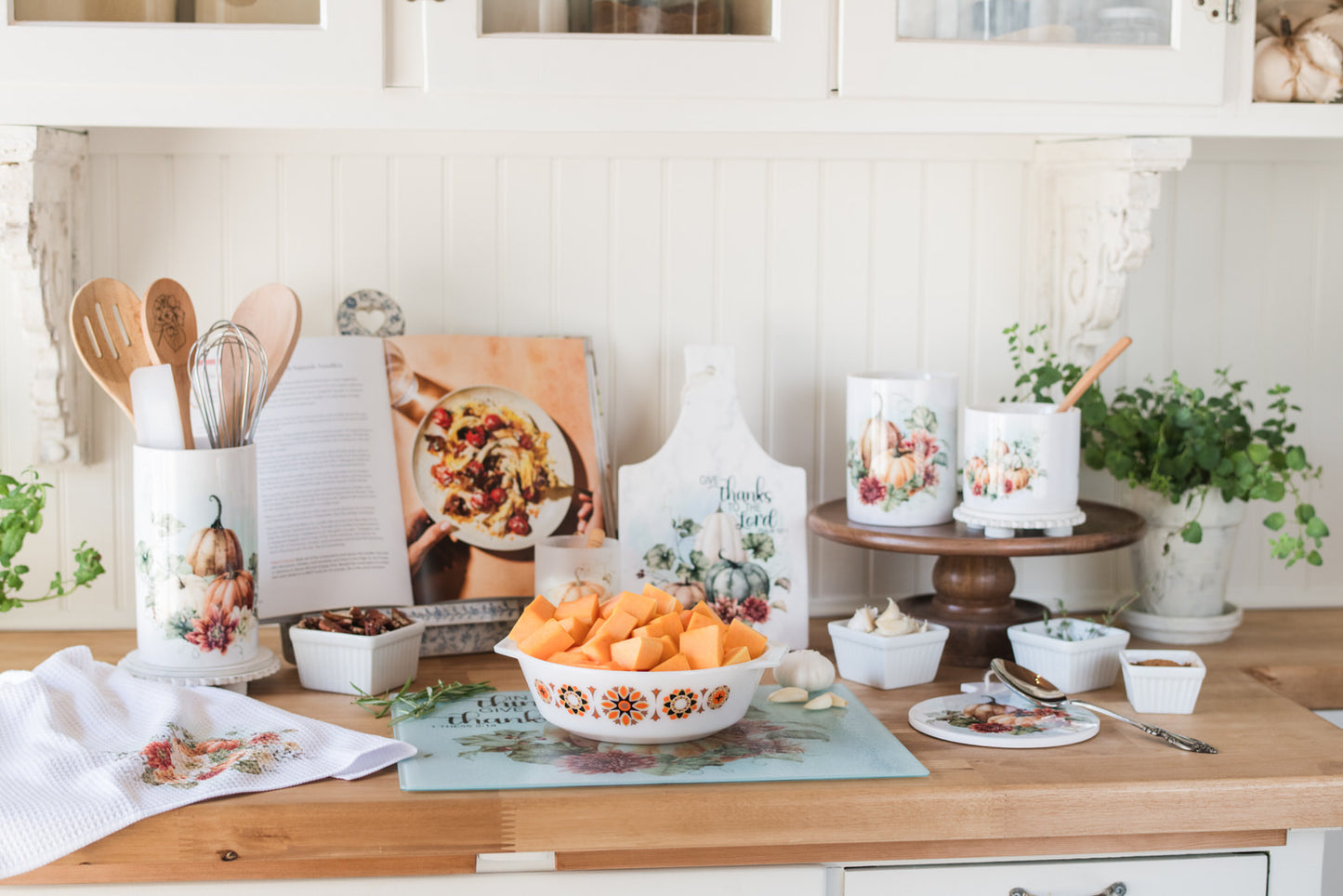 Kitchen counter with squash in a casserole dish on a glass cutting board and decorative autumn items on a wooden surface.