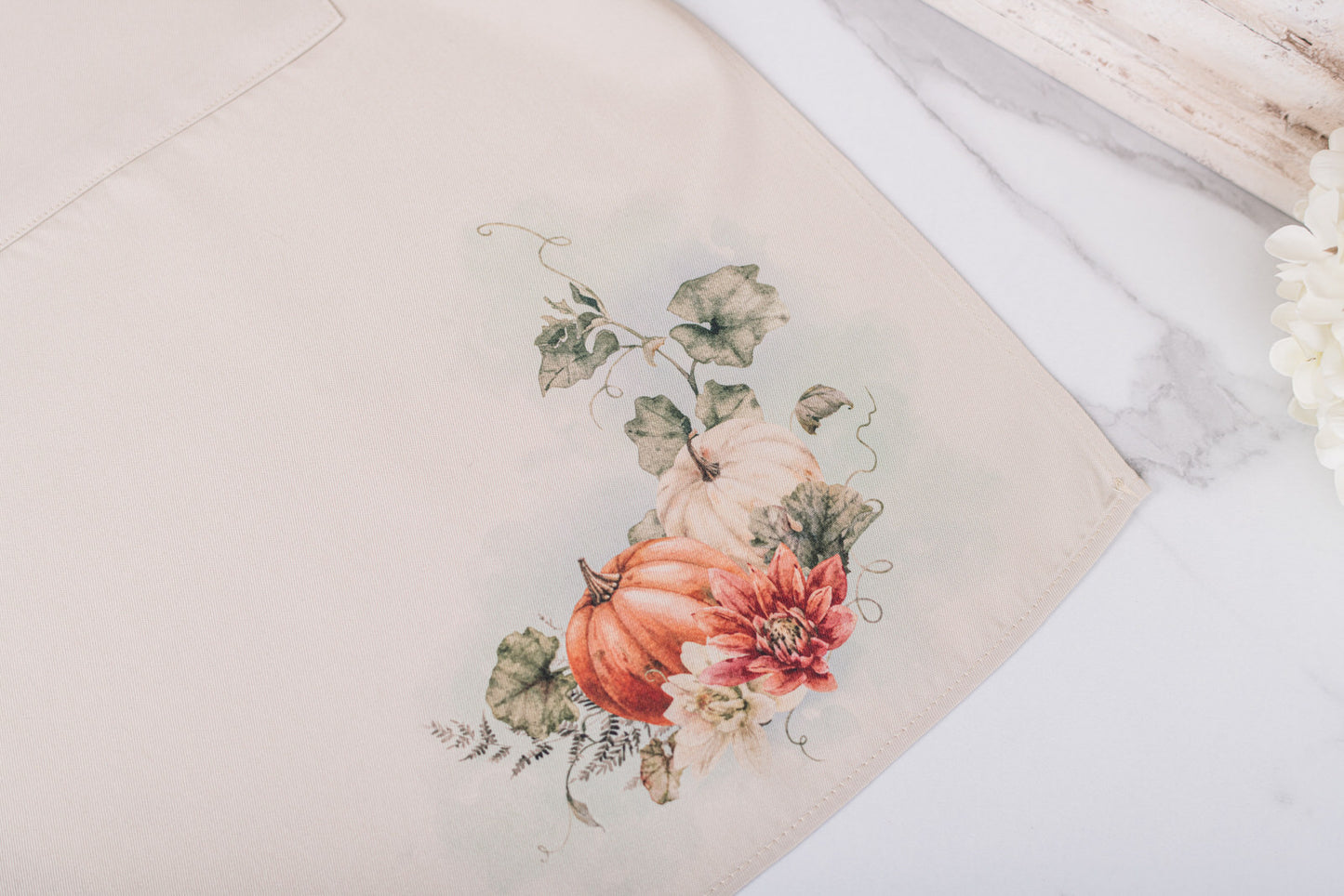 The lower corner of the beige kitchen apron with pumpkins and flowers