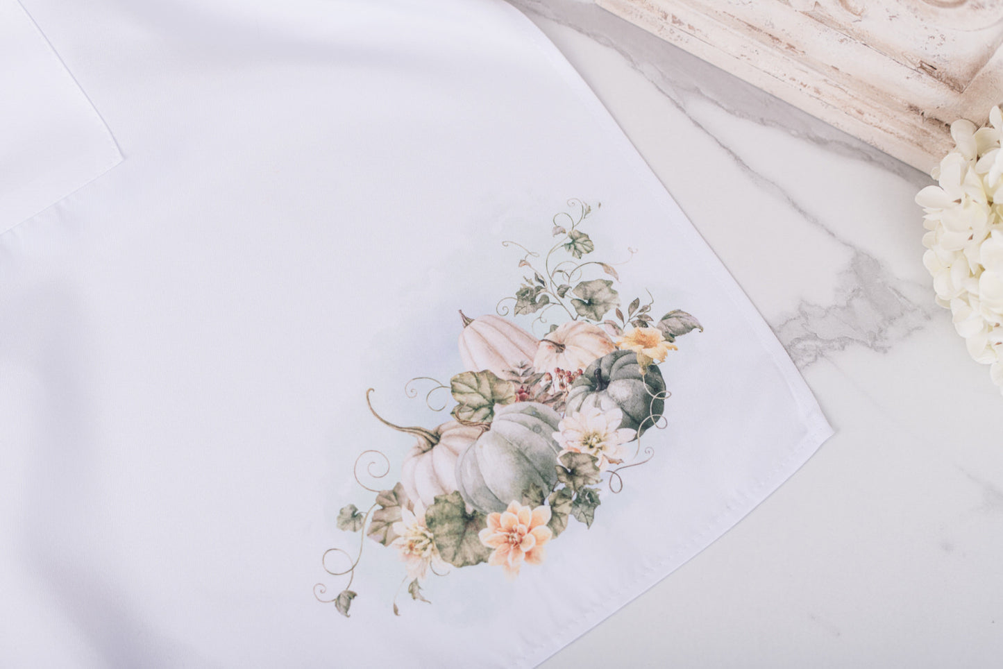 Floral and pumpkin design on a white apron in the lower corner