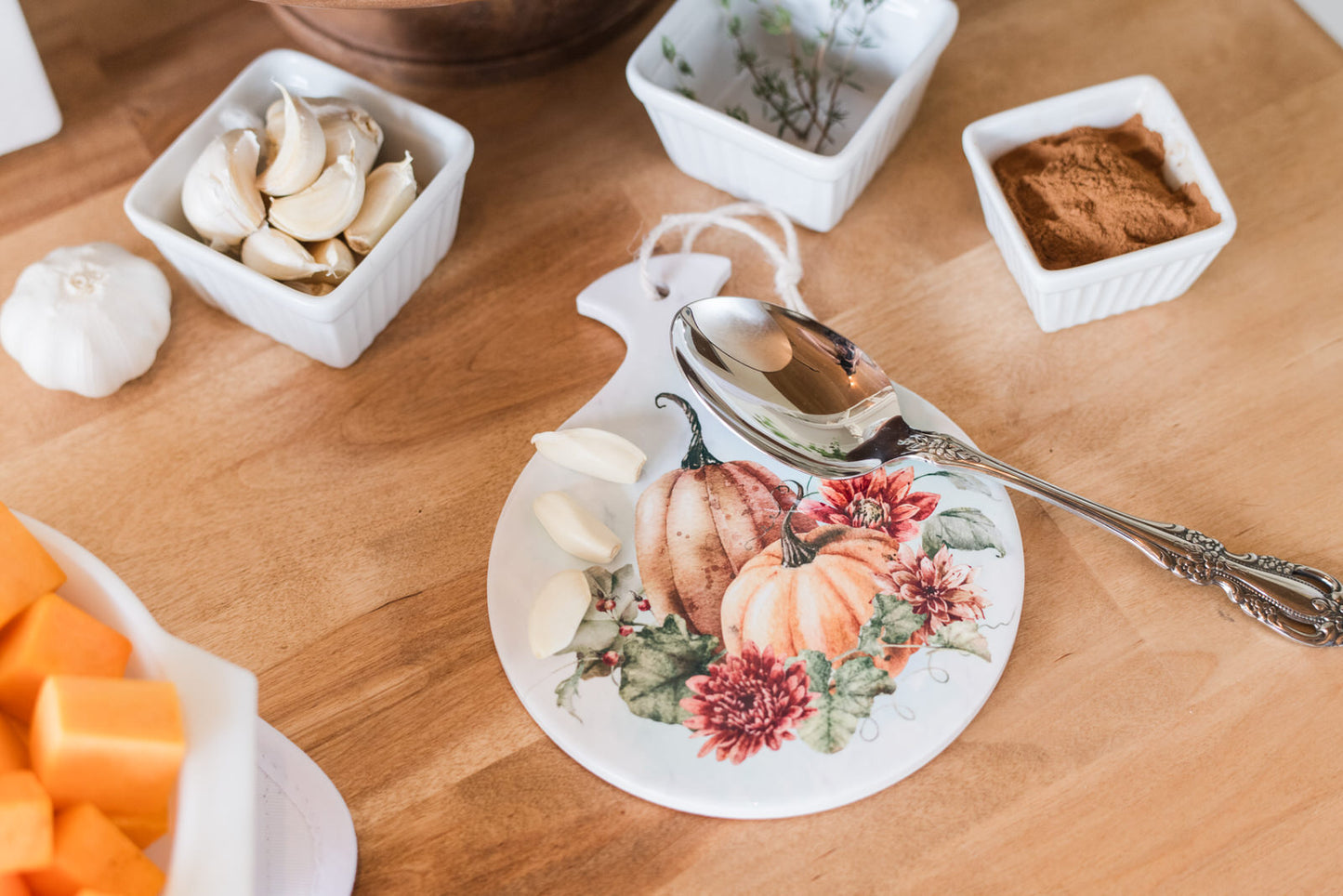 Spoon rest with pumpkins and flowers on a butcher block with food items.