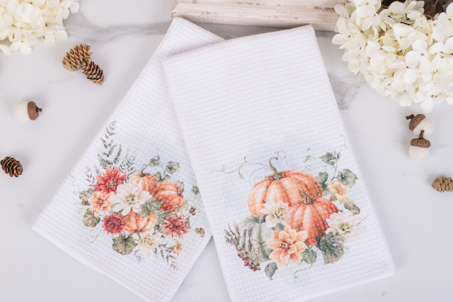 Two white towels with floral and pumpkin designs on a light background with decorative elements.