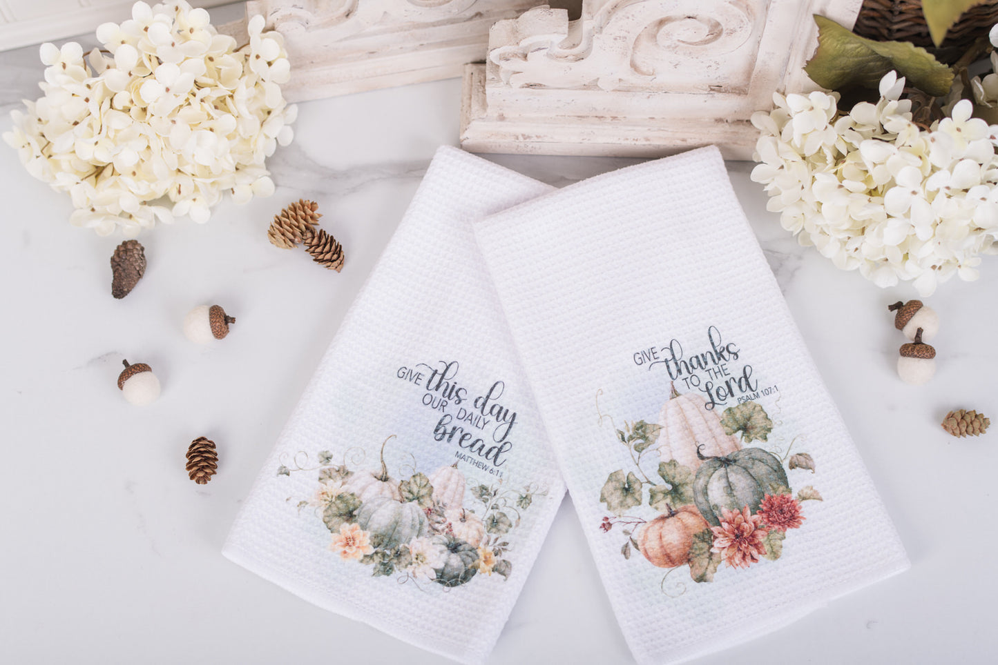Two decorative towels with floral designs and scripture on a white surface with decorative elements.