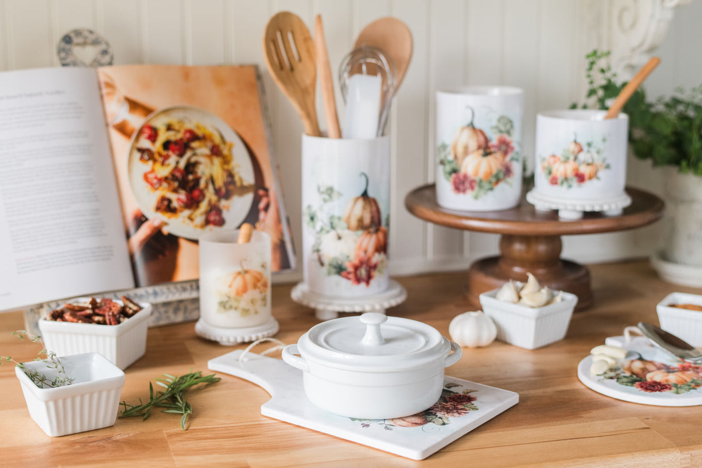 Decorative kitchen items including candles, a cookbook, and a white pot sitting on a trivet on a wooden table.