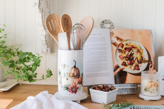 Kitchen utensils in a holder with a cookbook open on a wooden table.