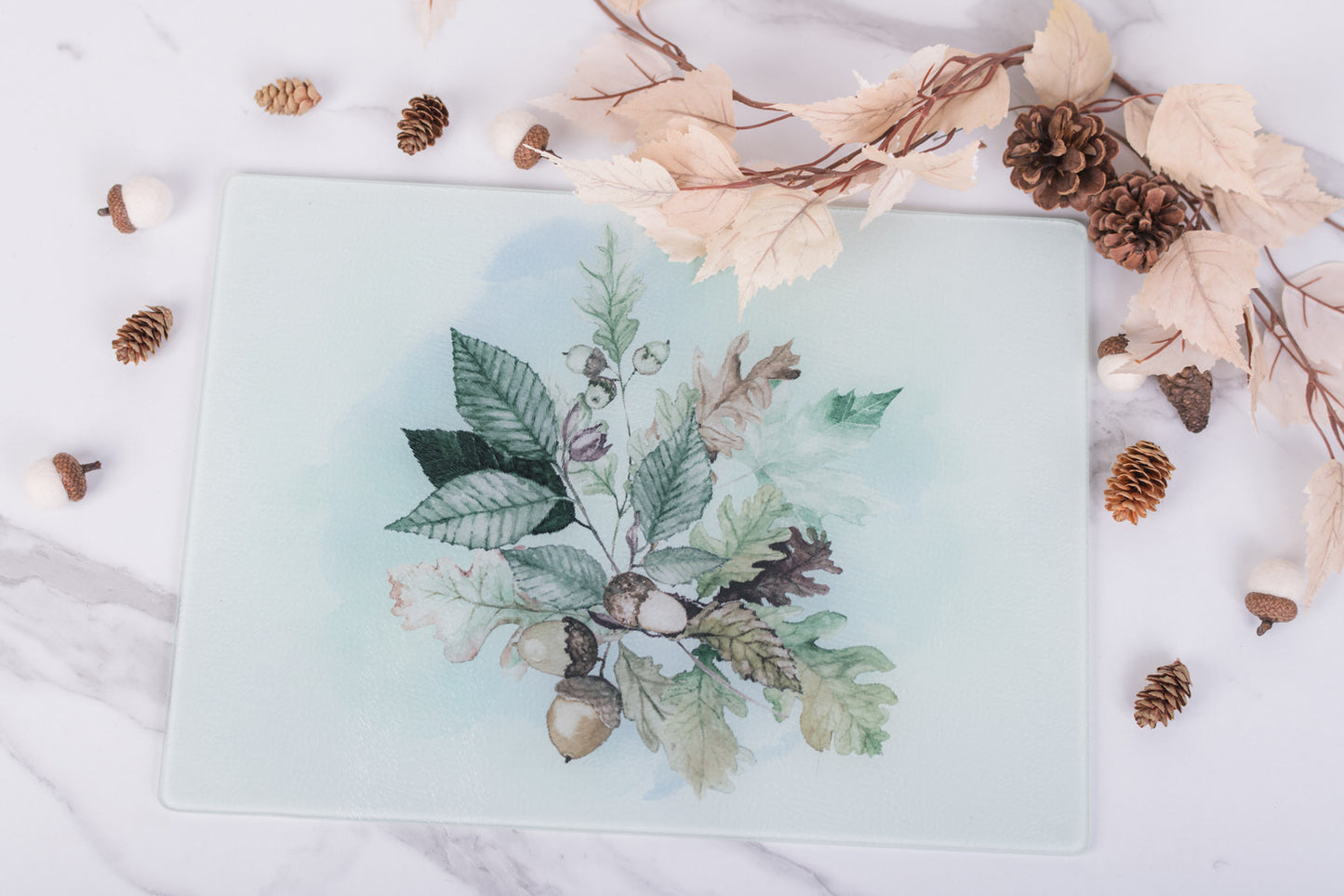 Decorative glass cutting board with leaf and acorn design on a white surface with decorative elements
