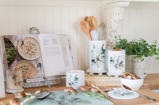 Kitchen counter with cookbooks, utensils, and decorative items on a light wooden surface.