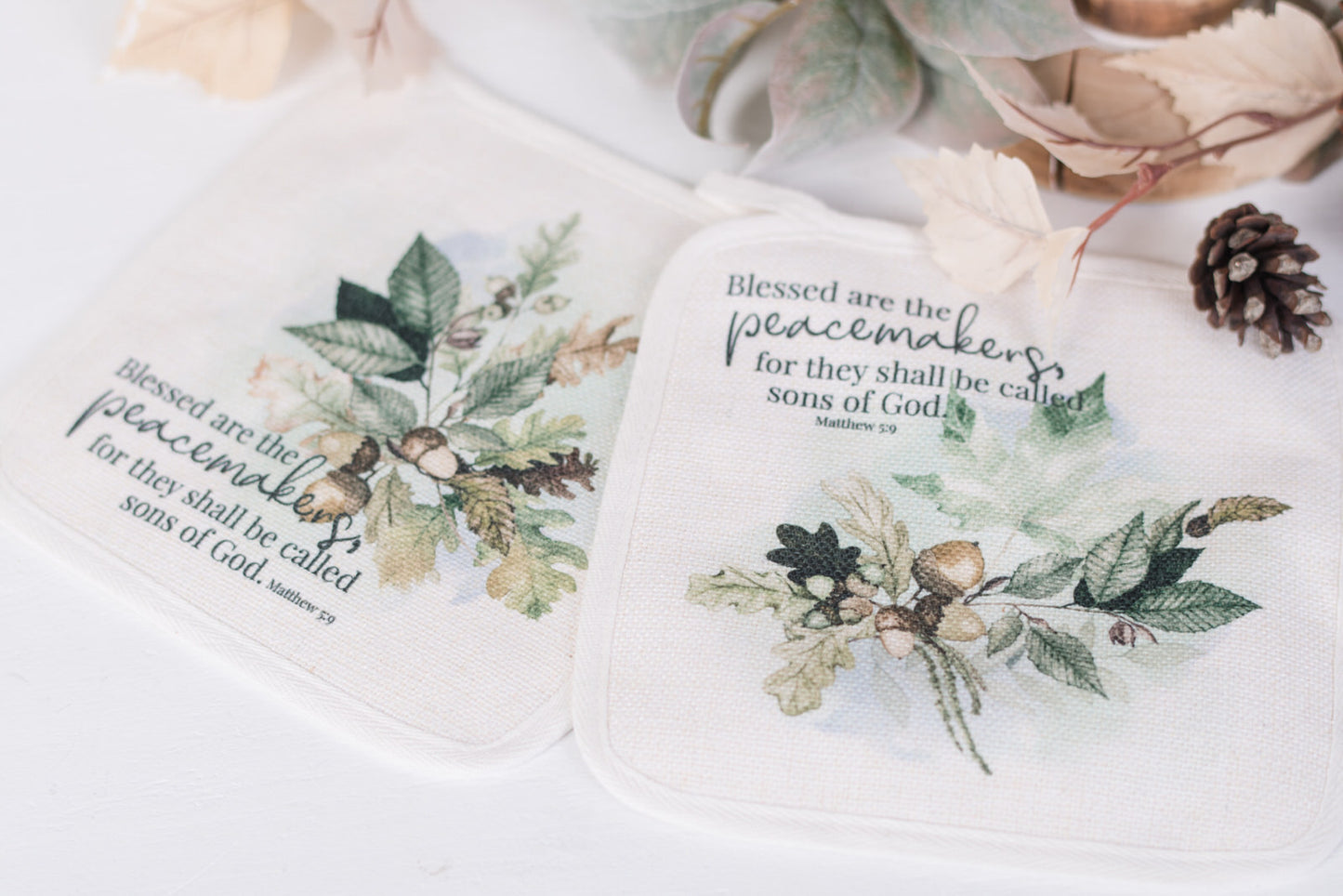 Two potholders with fall designs and Bible verse text on a white surface.