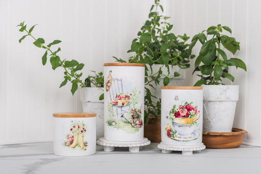 Decorative canisters with floral designs on a white surface with plants in the background