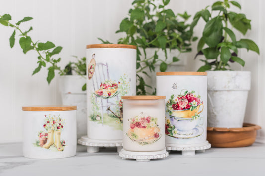 Decorative canisters with floral designs on a white surface with plants in the background