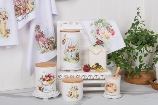 Decorative kitchen set with towels, jars, and a candle featuring floral and fruit designs.