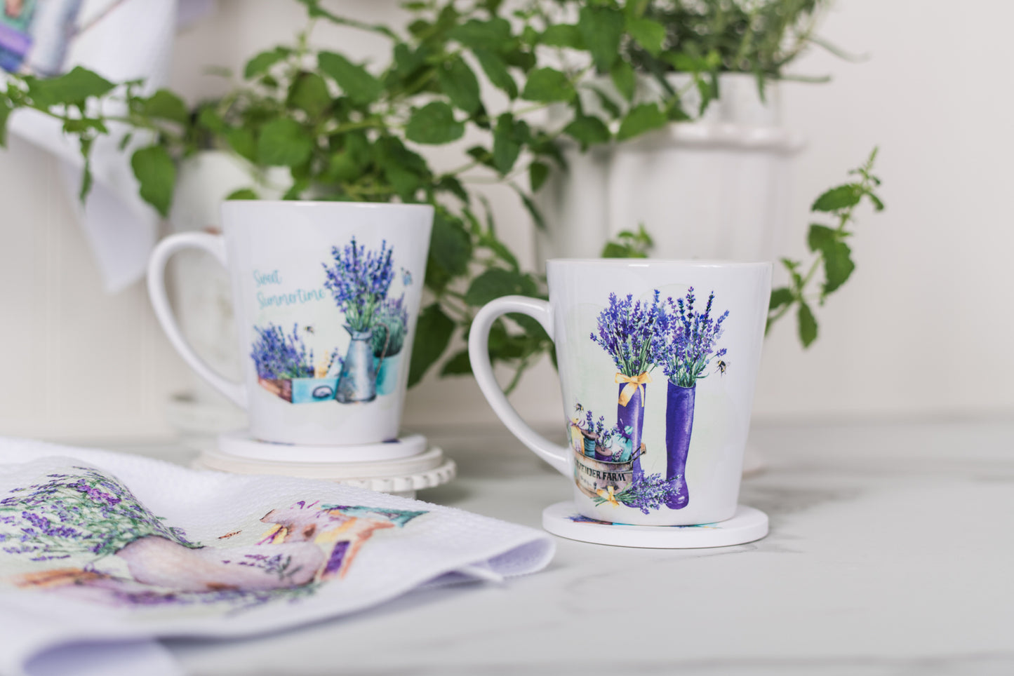 Two mugs with floral designs on a white surface with greenery in the background