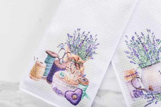 Two towels with designs of lavender and sewing tools on a white background.