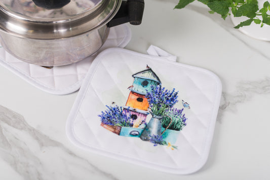White pot holder with colorful birdhouse and lavender design on a marble surface.