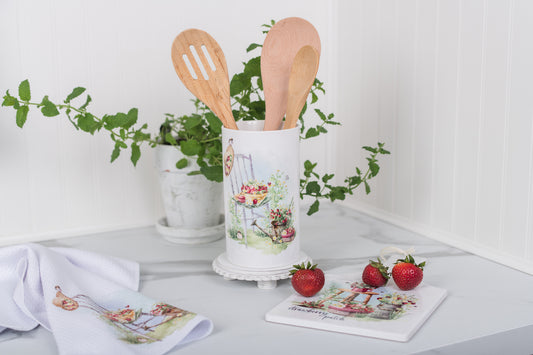 Kitchen utensil holder with wooden spoons on a kitchen counter with strawberries and a plant in the background.