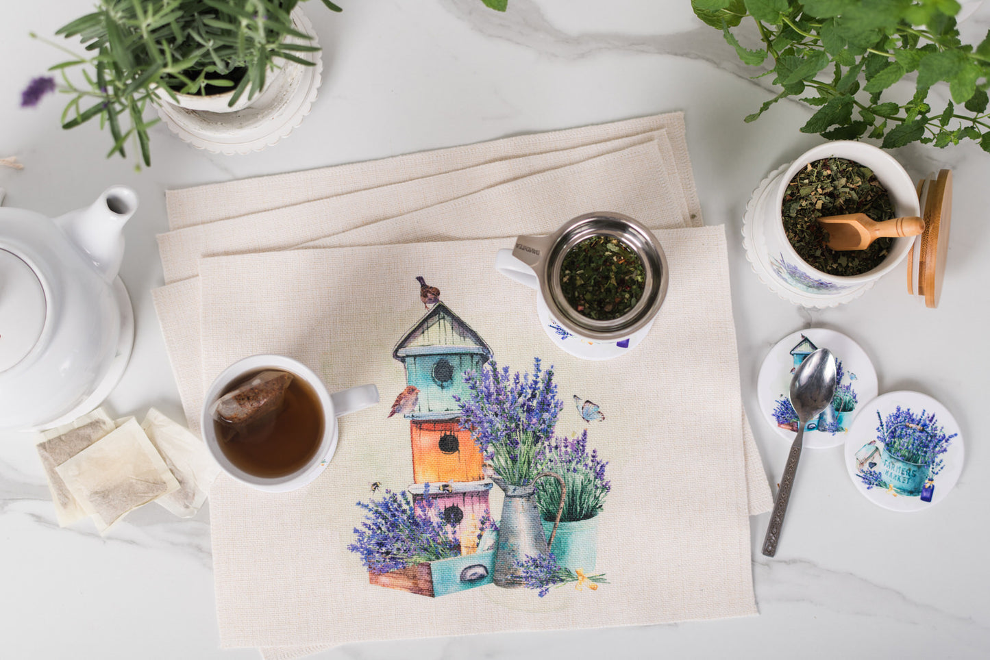 Tea set with a decorative mat featuring birdhouses and lavender on a white surface.