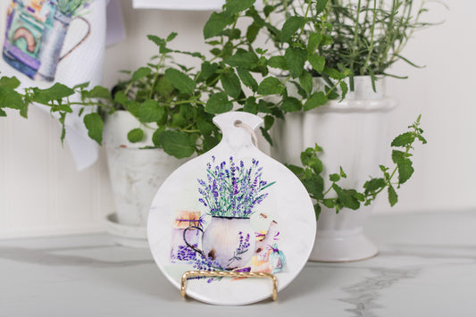 Decorative trivet with floral design on a stand, surrounded by green plants in white pots.