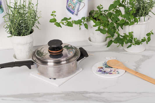 Stovetop with a pressure cooker, wooden spoon, and potted plants on a marble countertop.