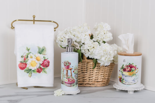 Bathroom set with fruit and floral-themed towels, soap dispenser, and tissue holder on a light background