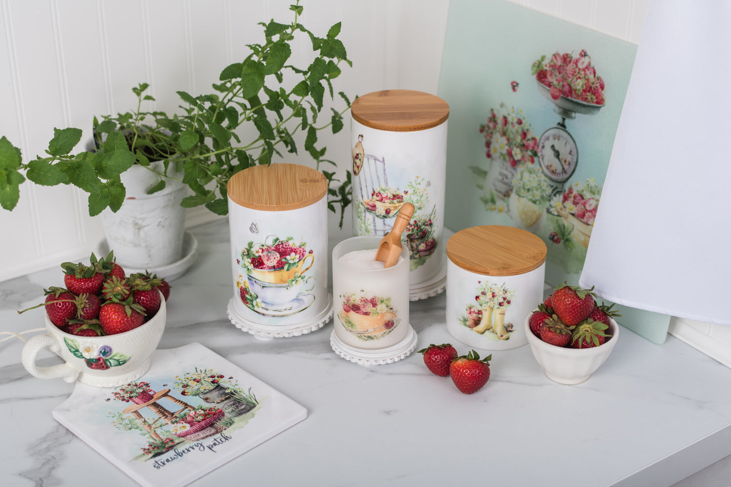 Decorative kitchen canisters with floral designs on a marble surface with strawberries and a plant.