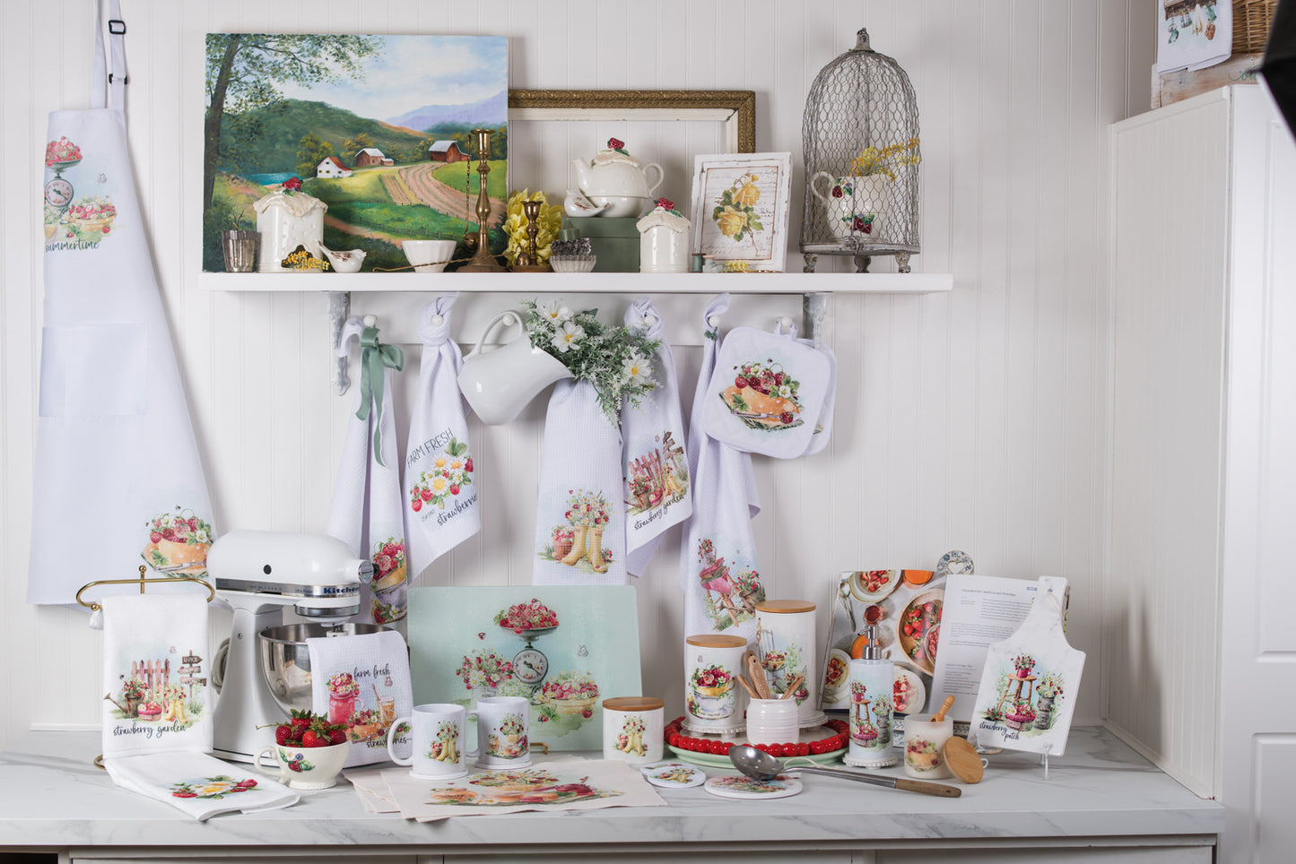 Kitchen decor with teapots, mugs, and kitchen towels featuring floral and strawberry designs on a white shelf.