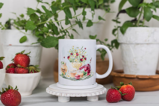 White mug with floral design on a small round stand, surrounded by strawberries and plants.