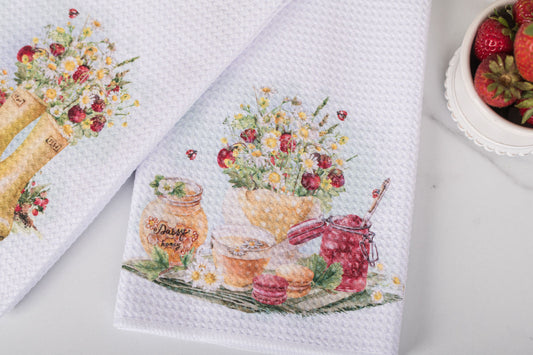 Decorative kitchen towels with floral and jar designs on a white surface.